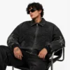 men-wearing-custom-jean-jacket Men's custom jean jacket styled for streetwear, featuring black washed denim, front zipper closure, artistic embroidery, sleeve patches, ribbed waistband and cuffs.