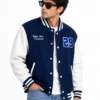 Man wearing a blue varsity jacket with white leather sleeves, striped ribbed collar and cuffs, snap buttons, embroidered chest name and number 29 varsity patch.