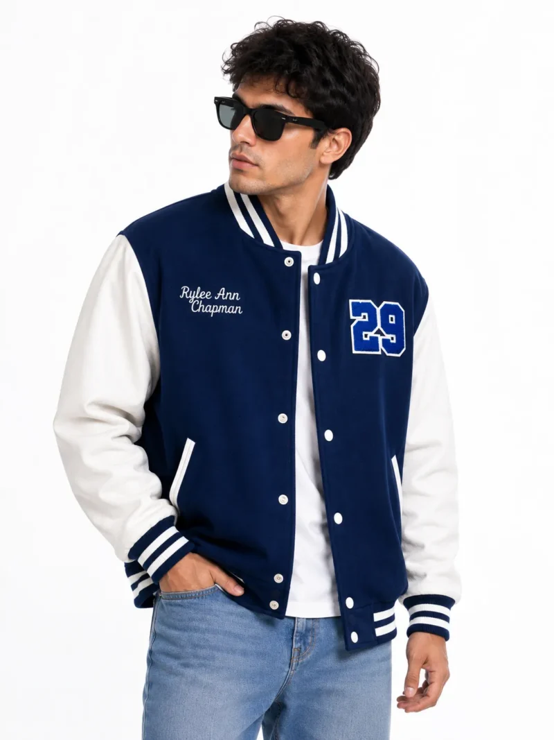 Man wearing a blue varsity jacket with white leather sleeves, striped ribbed collar and cuffs, snap buttons, embroidered chest name and number 29 varsity patch.