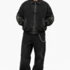 mens-custom-jean-jacket-streetwear Man wearing a custom jean jacket made from washed black denim, featuring a front zipper, embroidered artwork, decorative sleeve patches, ribbed cuffs and a modern streetwear fit.