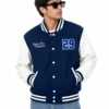 Men’s blue varsity jacket styled for streetwear, featuring white leather sleeves, striped ribbing, snap button closure, custom embroidery and classic varsity-inspired detailing.
